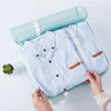 A light blue shirt is shown inside a teal travel storage organizer set being held by hands.