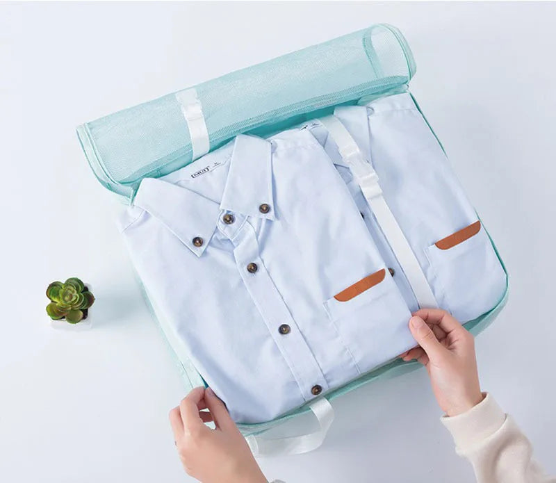A light blue shirt is shown inside a teal travel storage organizer set being held by hands.