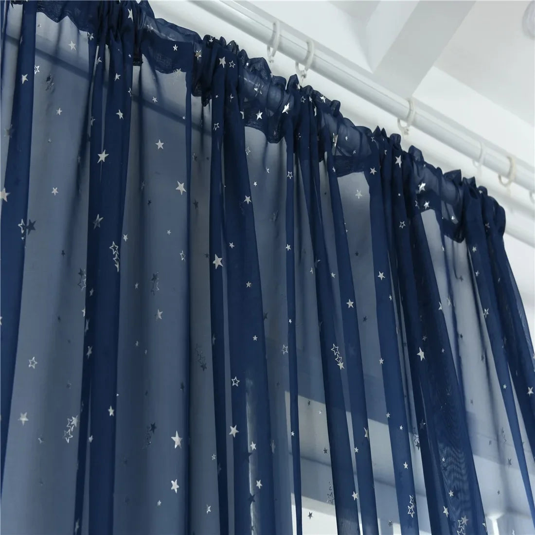 Blue sheer tulle curtains decorated with silver stars hanging in a window.