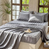 Gray satin bedding set draped on a bed with natural light streaming through large windows.