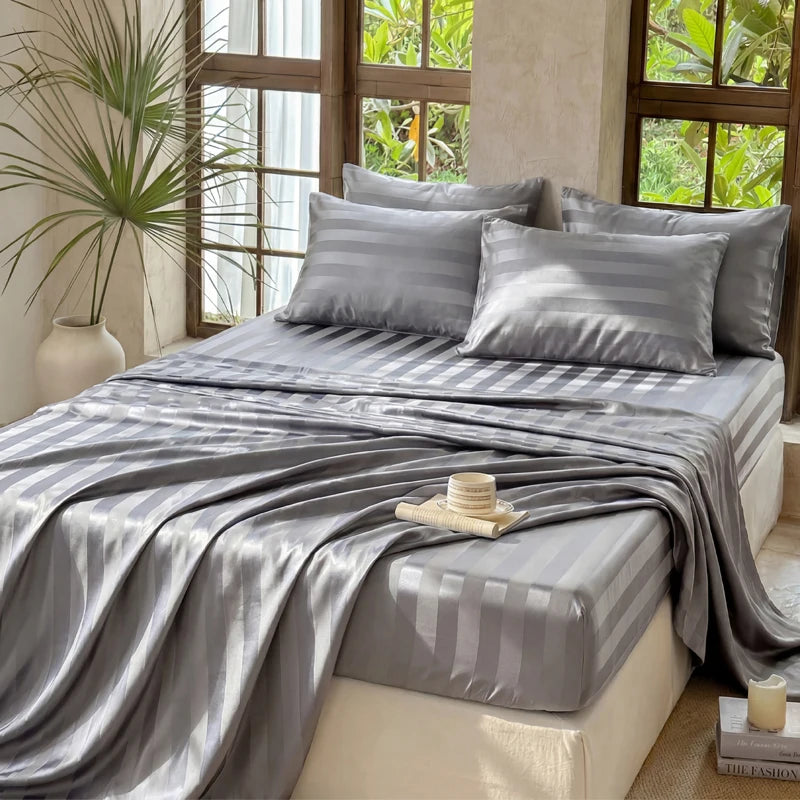 Gray satin bedding set draped on a bed with natural light streaming through large windows.