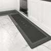 A rectangular black non-slip floor mat placed on a white marble floor near a cabinet.