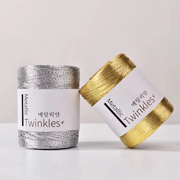 A roll of metallic twinkles yarn in a white container with gold-colored wrapping.