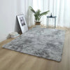 A thick gray faux fur area rug placed on a light wood floor next to a potted plant and a small table.