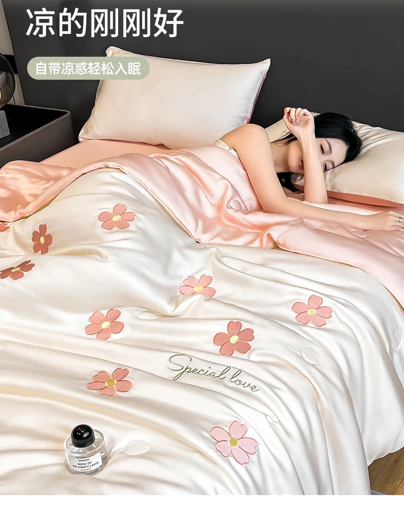 A pink satin quilt with floral embroidery is shown on a bed, suggesting a cooling summer sleep product.