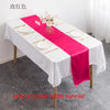 A pink satin table runner is displayed on a white tablecloth set for a formal dining or event.