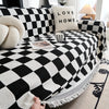 A black and white checkerboard sofa slipcover with a cream pillow and decorative throw on a light rug.