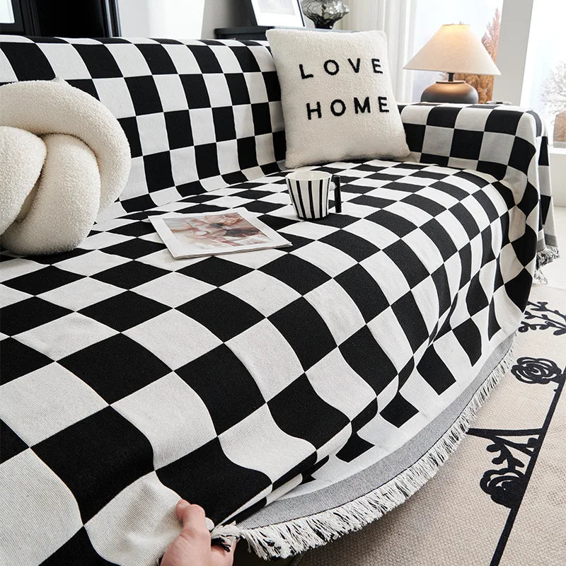 A black and white checkerboard sofa slipcover with a cream pillow and decorative throw on a light rug.