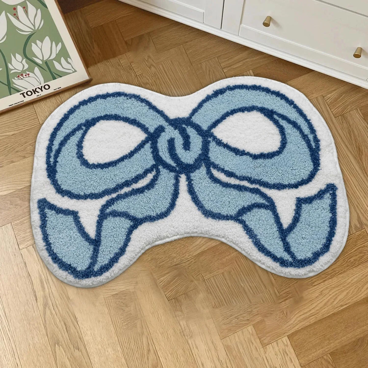 A light blue and white fluffy decorative rug shaped like a bow, placed on a wooden floor.