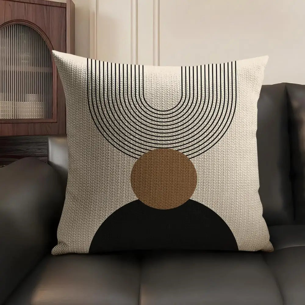 A beige cushion cover featuring black geometric lines and a circular brown accent on a dark gray sofa.