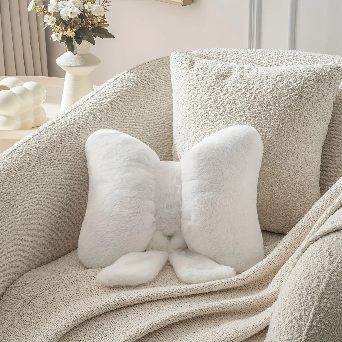 A close-up of a white fluffy decorative bow pillow resting on a beige knitted fabric sofa.