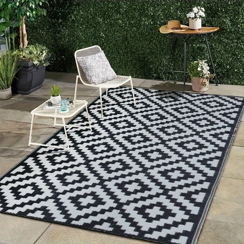 A black and white geometric outdoor rug placed on a patio with potted plants and a small side table.