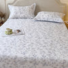 A floral printed cotton fitted sheet with a white background is displayed on a bed with a upholstered headboard.