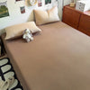 A beige quilt bed with light pink pillows and a small white stuffed animal on the bed.