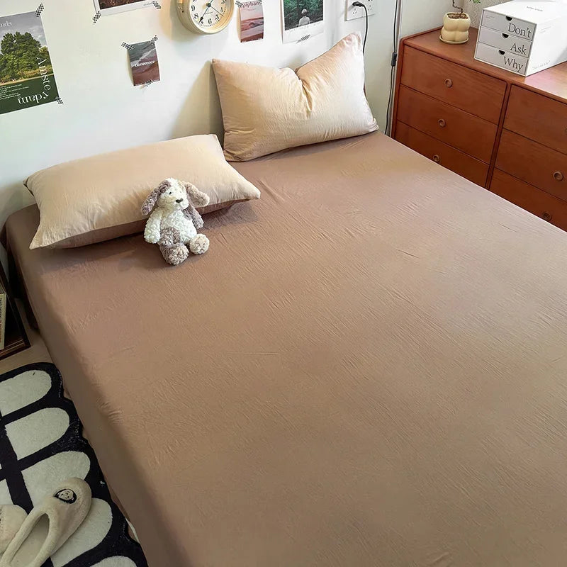 A beige quilt bed with light pink pillows and a small white stuffed animal on the bed.
