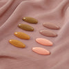 Eight plastic safety pins in various shades of beige and pink laid on a pink fabric.