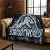A dark gray and white graphic blanket featuring a Jurassic World dinosaur design draped over a leather sofa.