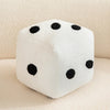 A white plush dice cube with black dots resting on a light surface.