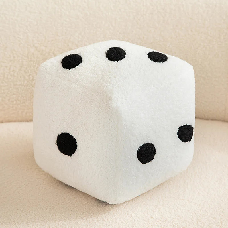 A white plush dice cube with black dots resting on a light surface.