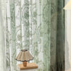 A set of romantic floral lace sheer curtains in a soft sage green color hanging in a window.