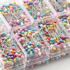 Assortment of decorative sewing and pinning needles in various colors and shapes packaged in clear plastic containers