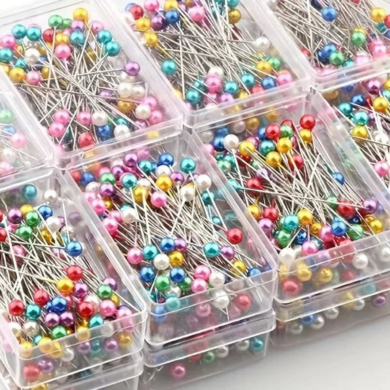 Assortment of decorative sewing and pinning needles in various colors and shapes packaged in clear plastic containers