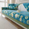 A teal and gold patterned jacquard sofa seat and back cover with white pillows in a bright room.
