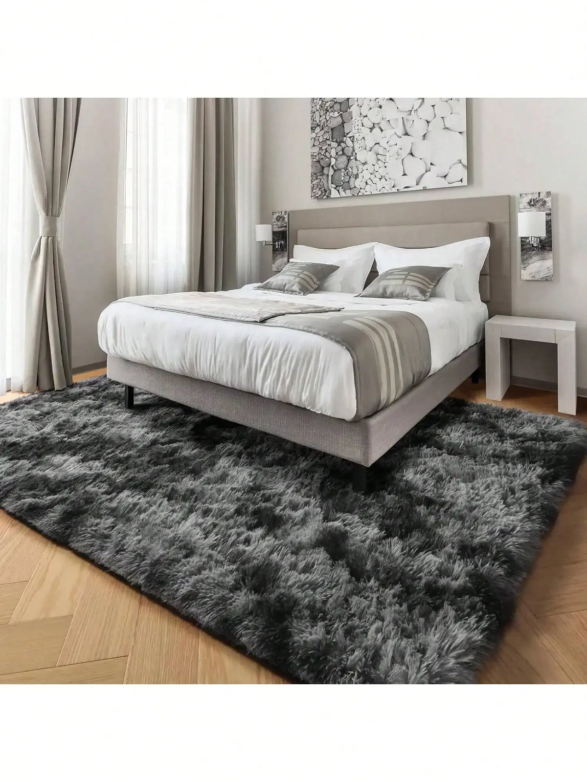 A plush long-pile area rug in dark gray and black lies on a wooden floor in front of a modern bed.