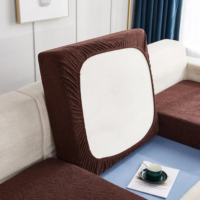 A close-up of a brown waterproof jacquard stretch sofa cover featuring a white cushion on a light blue surface.