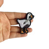 A hand holds a black and white embroidery patch of a duck.