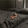 A dark gray linen flat sheet with a wooden cup and spoon resting on the fabric.