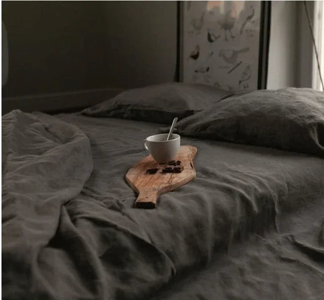 A dark gray linen flat sheet with a wooden cup and spoon resting on the fabric.