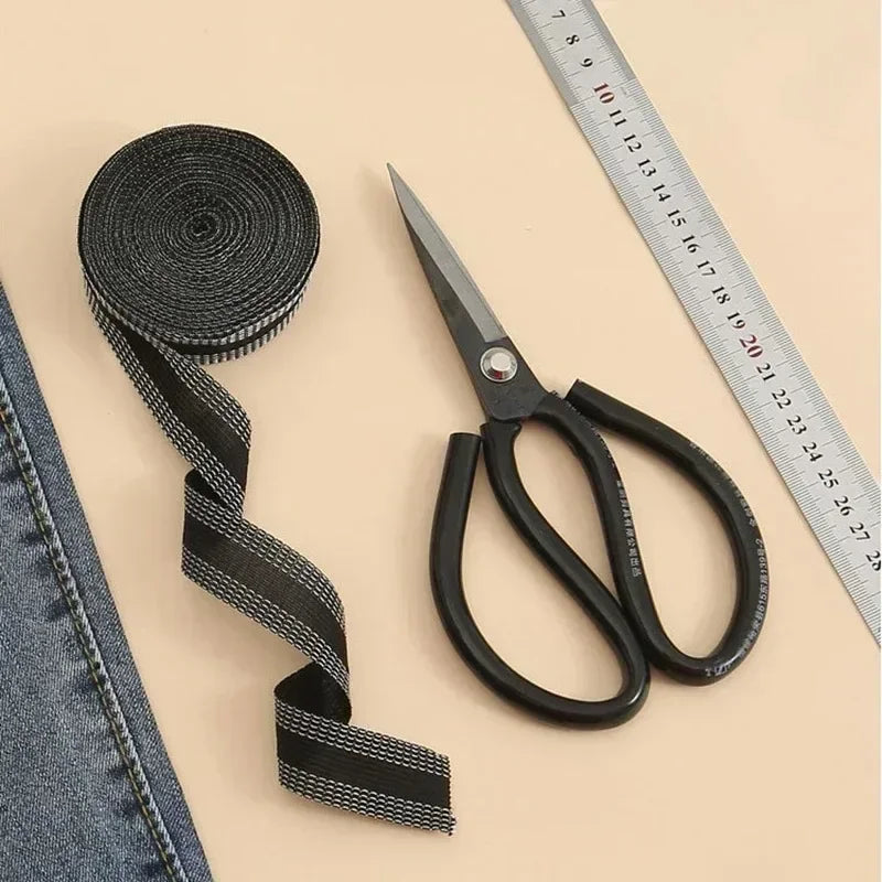 Black iron-on hem tape roll and pair of scissors shown next to a ruler on a beige surface