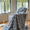 A gray plush faux fur throw blanket draped over a metal chair near a window.