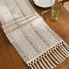 Beige boho hand-woven table runner with fringe displayed on a wooden table.