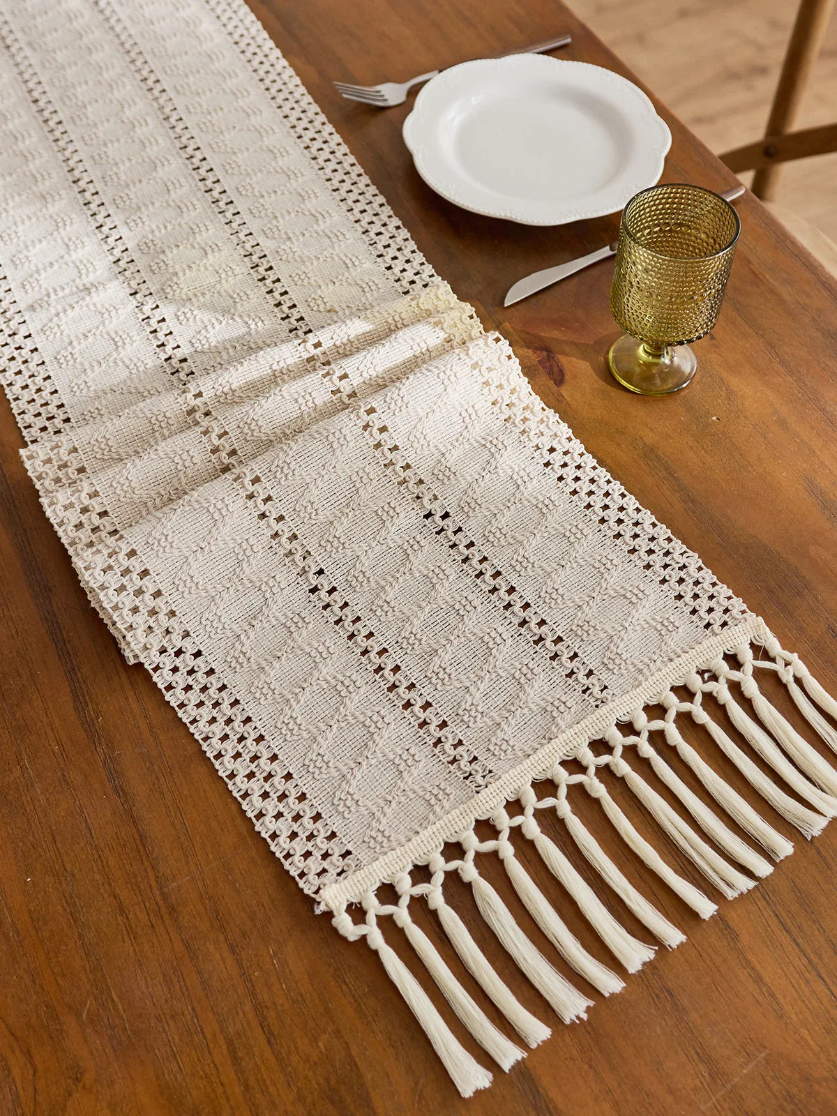 Beige boho hand-woven table runner with fringe displayed on a wooden table.