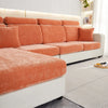 An orange stretchable chenille sofa cushion cover on a white sofa with light wood accents.