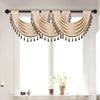 A beige European style window curtain valance with tassels hanging over a window.