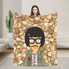 A person holds up a throw blanket featuring an anime-style character with black hair and glasses against a patterned backgrou