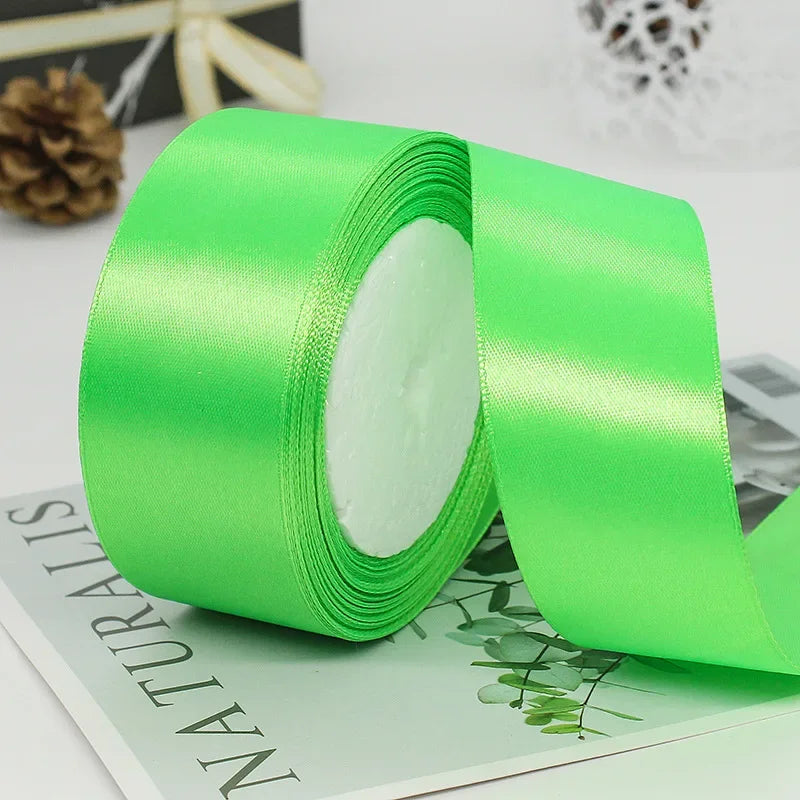A roll of bright lime green satin ribbon with white filling, placed on a green card.