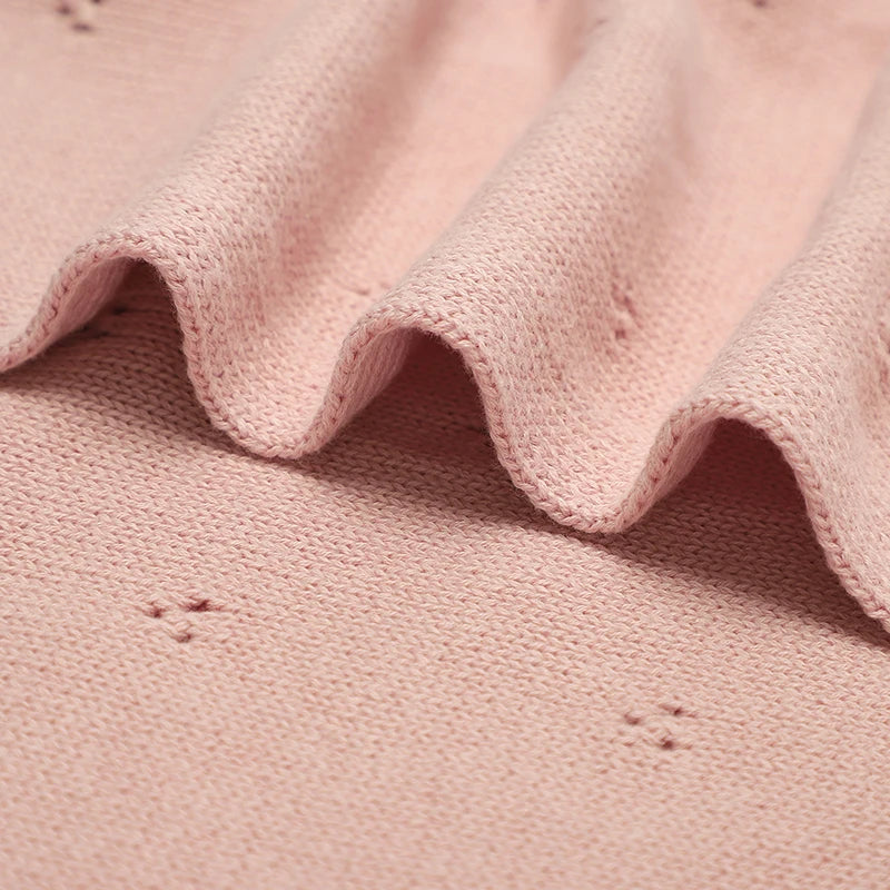 A close-up of a soft pink cotton knit baby blanket showing ruffled edges and texture.