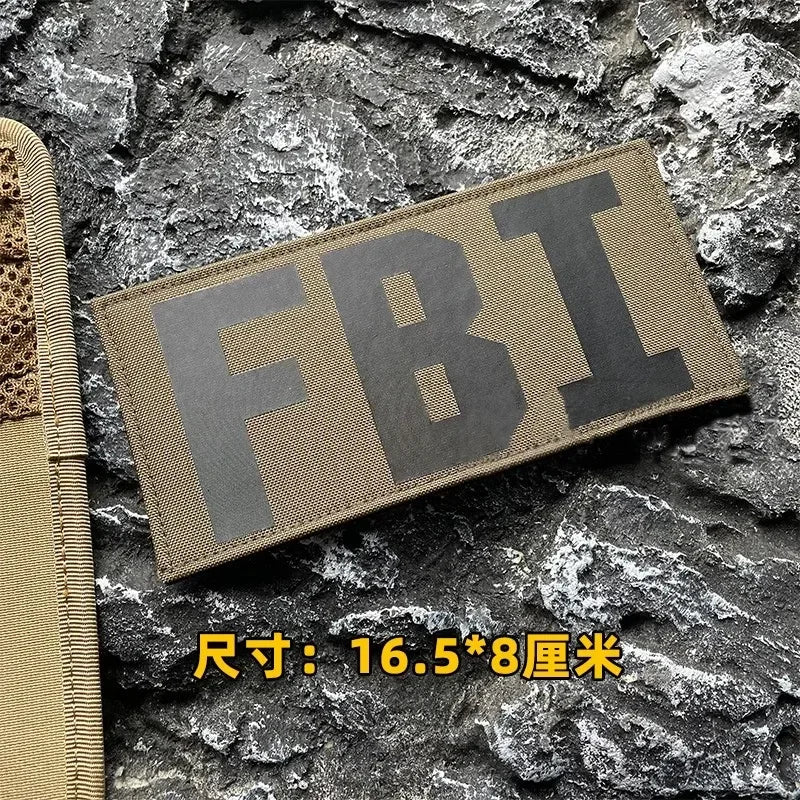 A dark olive tactical hook and loop patch with the letters FBI is displayed on a rough stone background.