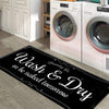 A black laundry mat with white text that reads Wash & Dry tomorrow placed on a wooden floor in front of white washing machine