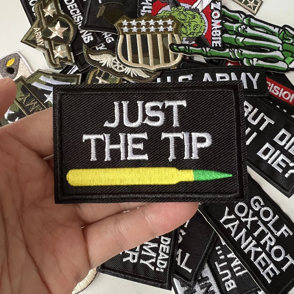 A black iron-on patch featuring the text JUST THE TIP and a yellow pencil design.