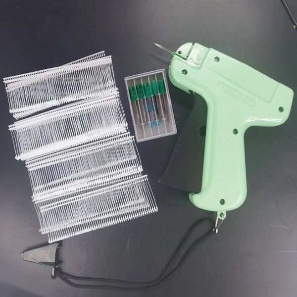 A light green precision sewing tag gun kit with multiple needles and a plastic holder is displayed on a dark surface.