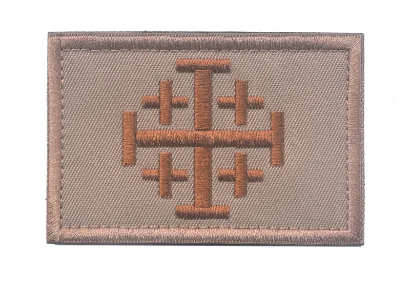 A rectangular embroidered patch in tan fabric featuring a brown cross design.