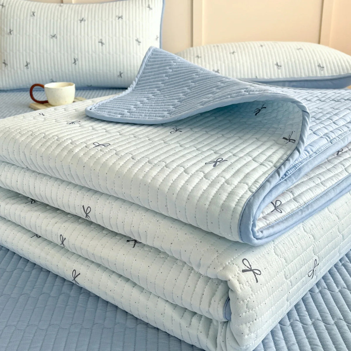 Light blue quilted bedspread with a subtle floral pattern stacked on a bed.