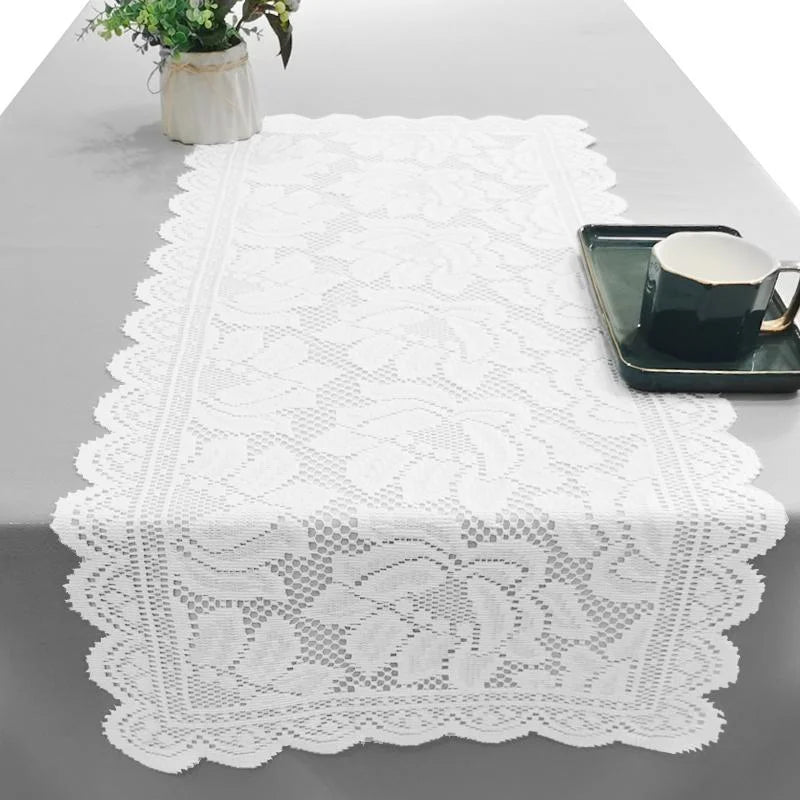 White lace table runner with scalloped edges on a gray table, featuring intricate floral patterns.