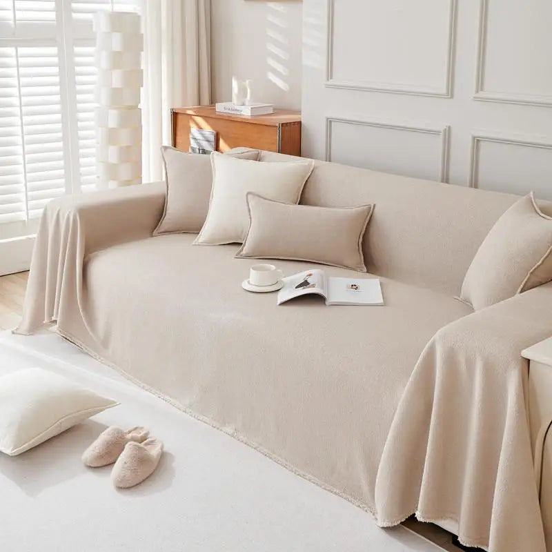 A beige anti-scratch sofa cover draped over a light-colored sofa with matching pillows and a book.