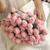 A handmade rose crochet blanket bouquet with a green gift bag resting on a white fabric surface.